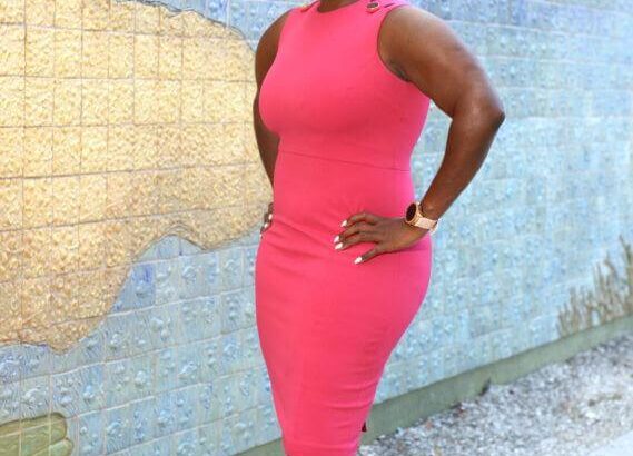 Woman in a fitted pink dress posing against a textured wall.